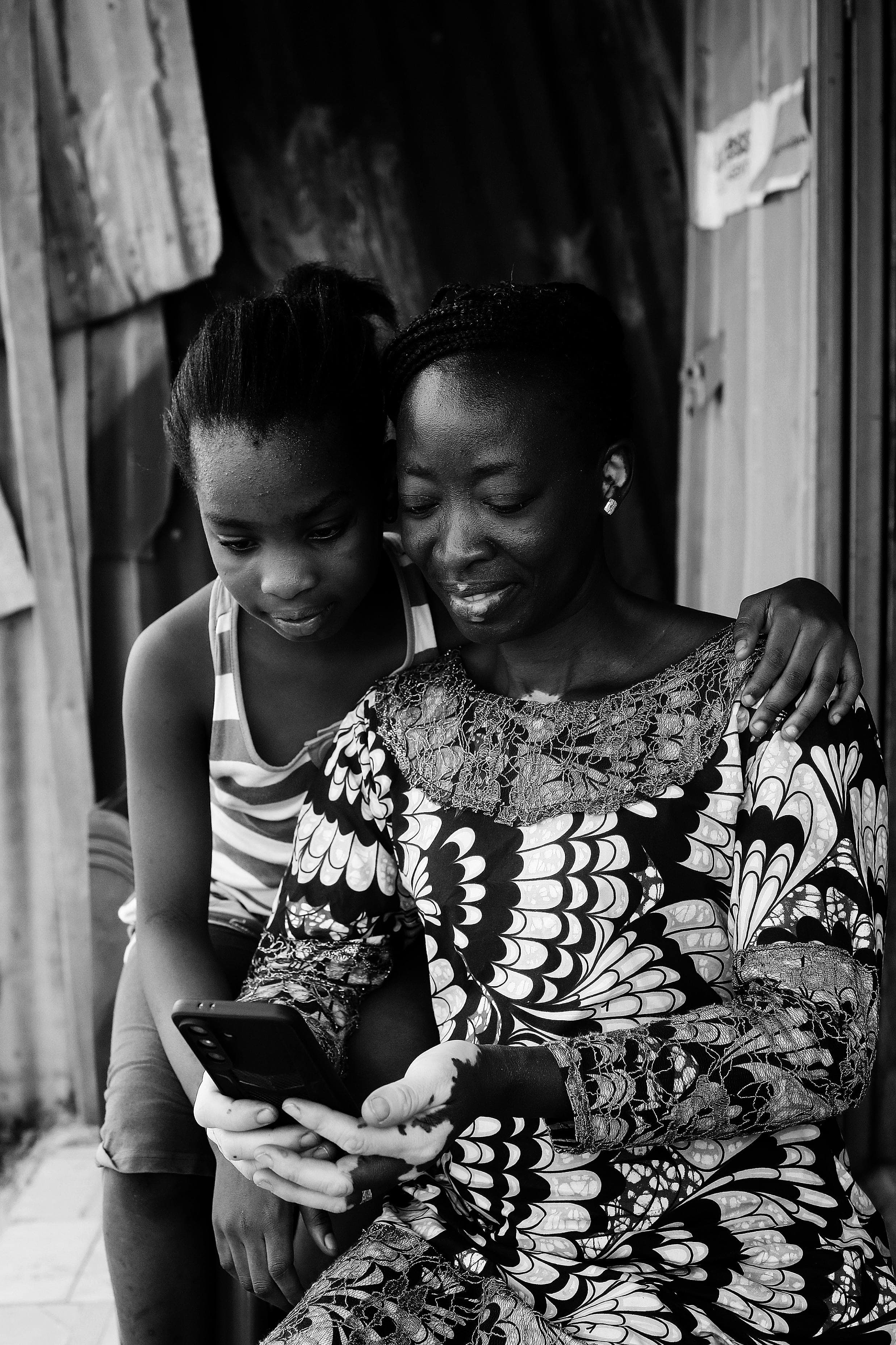 Femme et jeune fille regardant ensemble un téléphone devant une maison